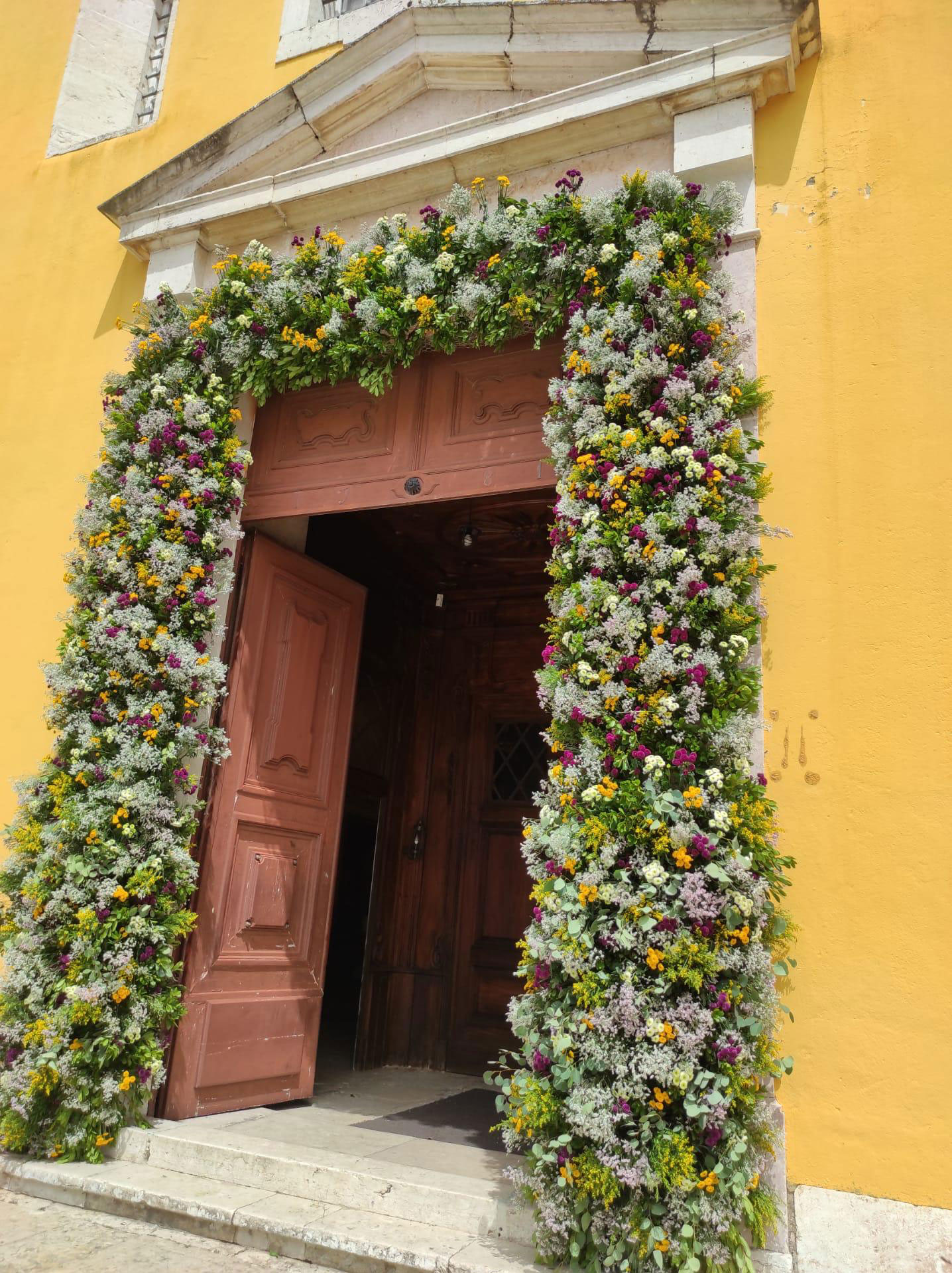 Arranjo na porta da igreja repleto de flores decorar e muitas folhagens.